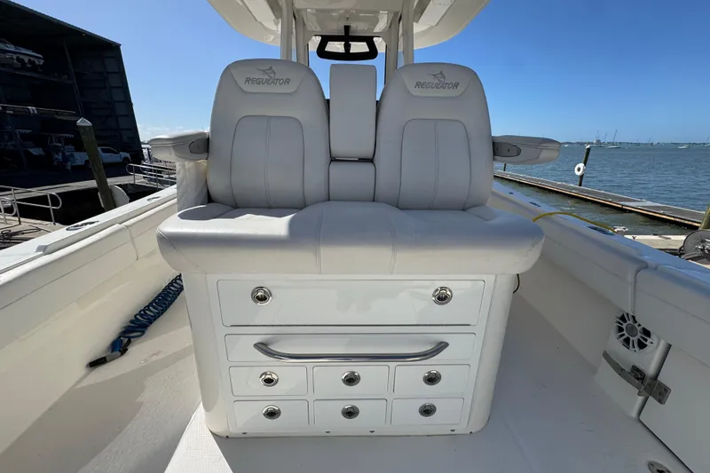 Slide: The Image of 2023 Regulator 31 boat interior with cushioned seating and storage drawers, docked by the water. - 8