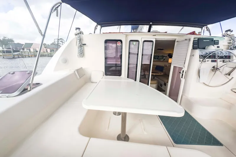 Slide: The Image of 2002 Leopard 42 catamaran cockpit with table, seating, and helm, docked by waterfront homes. - 6