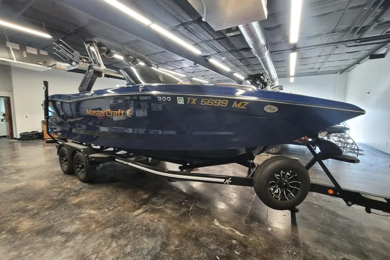 The Image of 2025 MasterCraft X24 boat on trailer in indoor showroom setting. - 1
