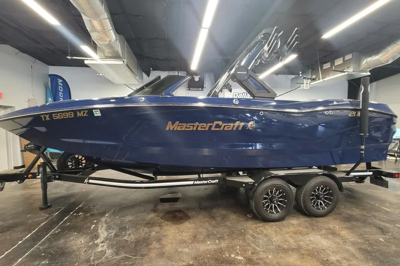 Slide: The Image of 2025 MasterCraft X24 boat in showroom, blue exterior, on trailer, side view. - 6