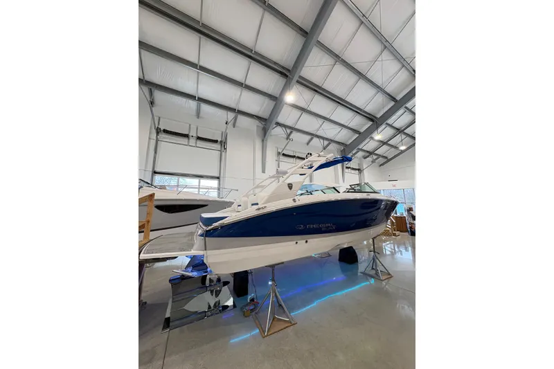 Slide: The Image of 2026 Regal LS6 Surf boat in showroom, blue and white design, elevated on stands. - 6