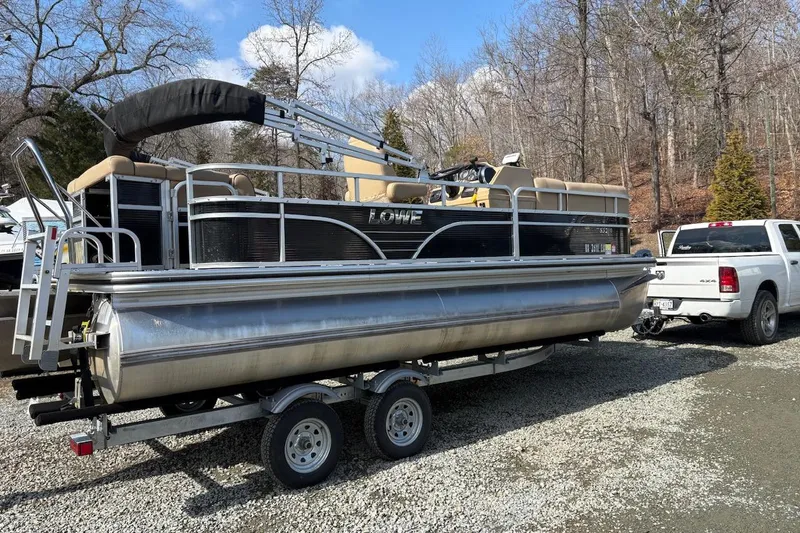 Slide: The Image of 2018 Lowe SS 210 pontoon boat on trailer, hitched to white truck in wooded area. - 2