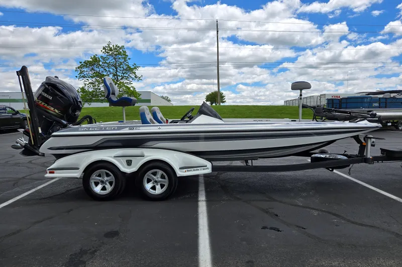 Slide: The Image of 2015 Skeeter FX20 bass boat on trailer, parked outdoors under a partly cloudy sky. - 4