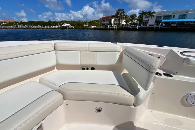 Slide: The Image of 2019 Pursuit S 368 Sport boat interior with white seating, docked by waterfront homes. - 10