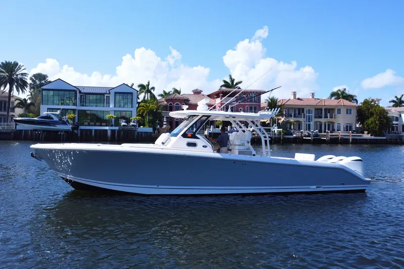 Slide: The Image of 2019 Pursuit S 368 Sport boat cruising near waterfront homes under a clear blue sky. - 42