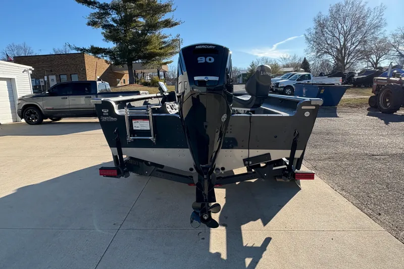 Slide: The Image of 2025 Lund 1875 Pro Guide boat with Mercury 90 engine, parked outdoors. - 2