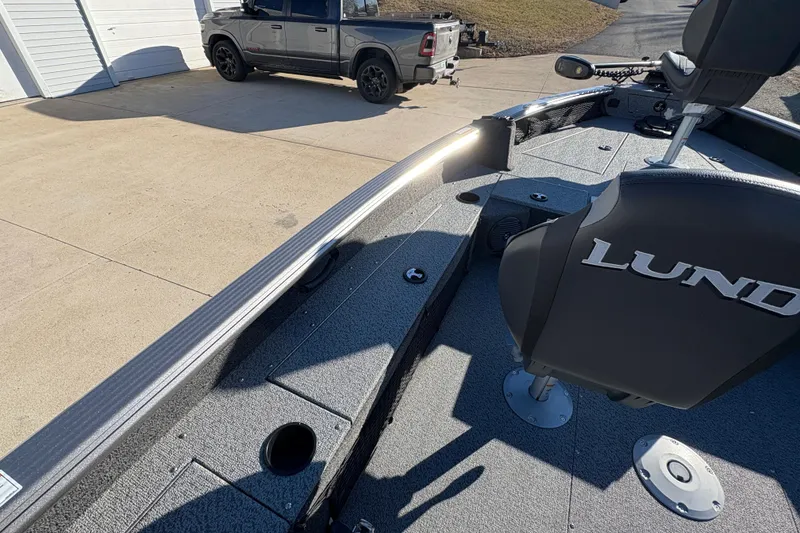 Slide: The Image of 2025 Lund 1875 Pro Guide boat interior with seating and storage, parked near a truck. - 24