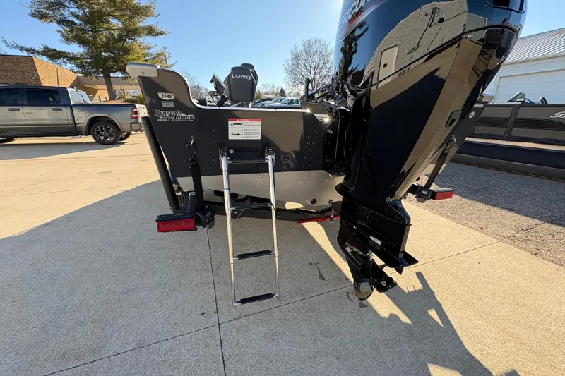 Slide: The Image of 2025 Lund 1875 Pro Guide boat rear view with ladder and motor in a driveway. - 37