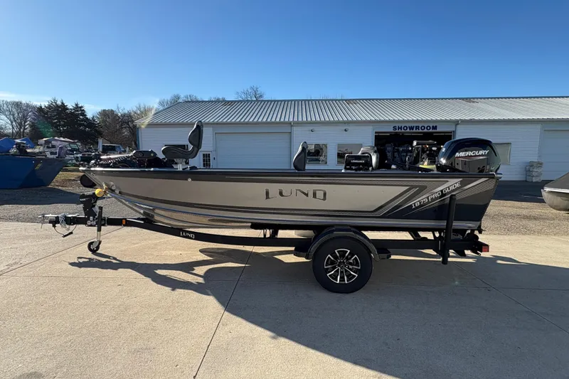 Slide: The Image of 2025 Lund 1875 Pro Guide boat on trailer outside showroom, sunny day. - 4