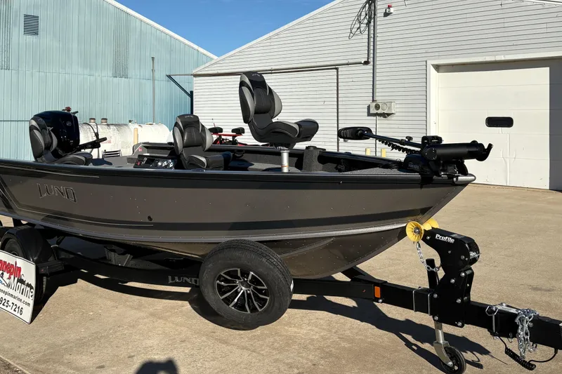 Slide: The Image of 2025 Lund 1875 Pro Guide fishing boat on trailer, parked outside industrial building. - 7