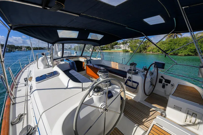 Slide: The Image of 2003 Beneteau 50 sailboat cockpit with dual steering wheels, docked in scenic waters. - 1