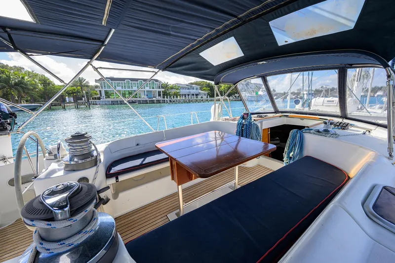 Slide: The Image of Beneteau 50 sailboat cockpit, 2003 model, with seating and table, docked by waterfront homes. - 18