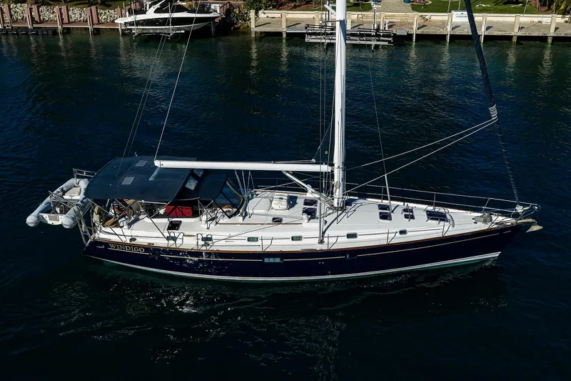 Slide: The Image of 2003 Beneteau 50 sailboat on water, side view, with dock and greenery in background. - 76
