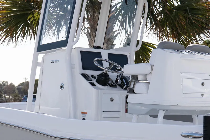 Slide: The Image of 2026 Caymas 26 HB boat console with steering wheel and seating, under palm tree. - 18