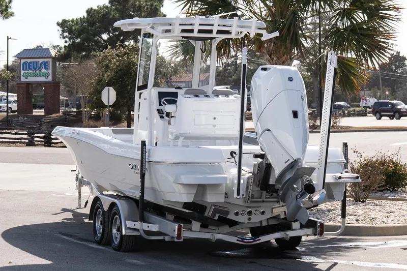 Slide: The Image of 2026 Caymas 26 HB boat on trailer, parked near palm trees and a shop. - 4