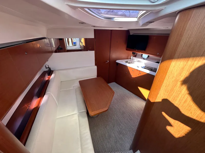 Slide: The Image of 2013 Beneteau Gran Turismo 38 interior with white seating, wooden table, and kitchenette. - 17