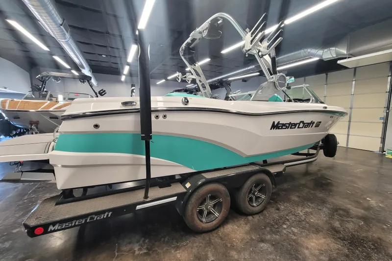 Slide: The Image of 2020 MasterCraft XT23 boat on trailer in showroom, featuring sleek design and teal accents. - 6