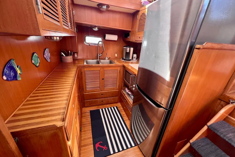 Slide: The Image of 1984 Kha Shing Spoiler yacht kitchen with wood cabinetry, stainless steel fridge, and nautical decor. - 11