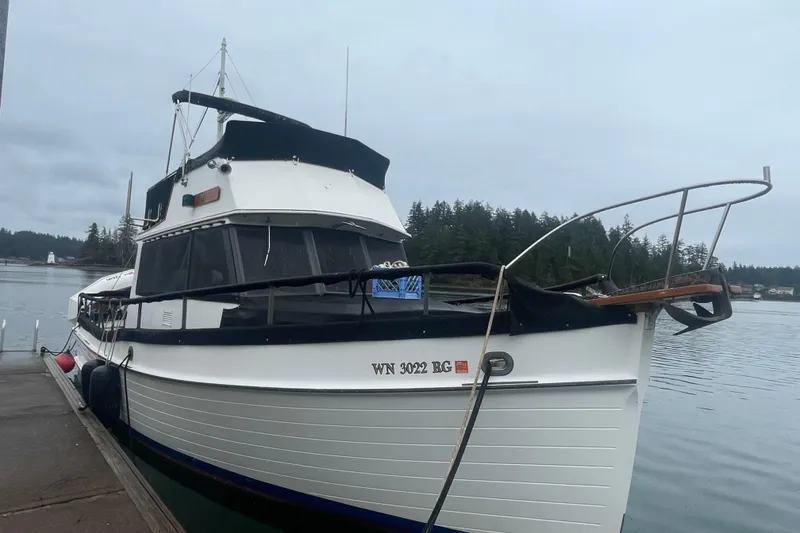 Slide: The Image of 1984 Grand Banks 32 Sedan docked by a serene waterfront with forested background. - 2