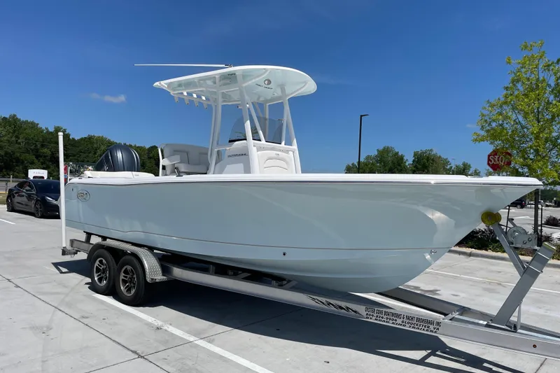 The Image of 2023 Sea Hunt Ultra 234 boat on trailer in parking lot under clear blue sky. - 0