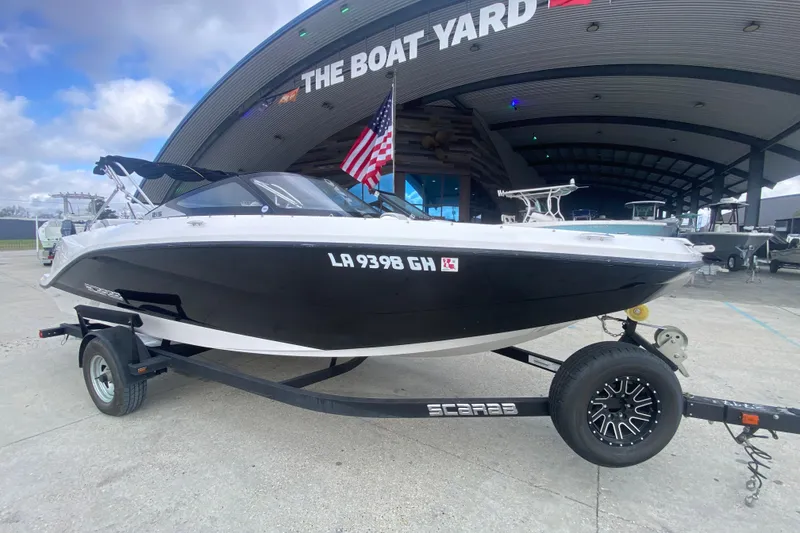 Slide: The Image of 2018 Scarab 215 G boat on trailer at The Boat Yard, featuring sleek black and white design. - 18
