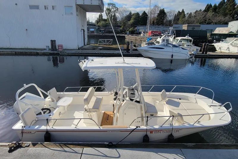 Slide: The Image of 2023 Boston Whaler 210 Montauk boat docked at a marina, surrounded by water and other boats. - 5