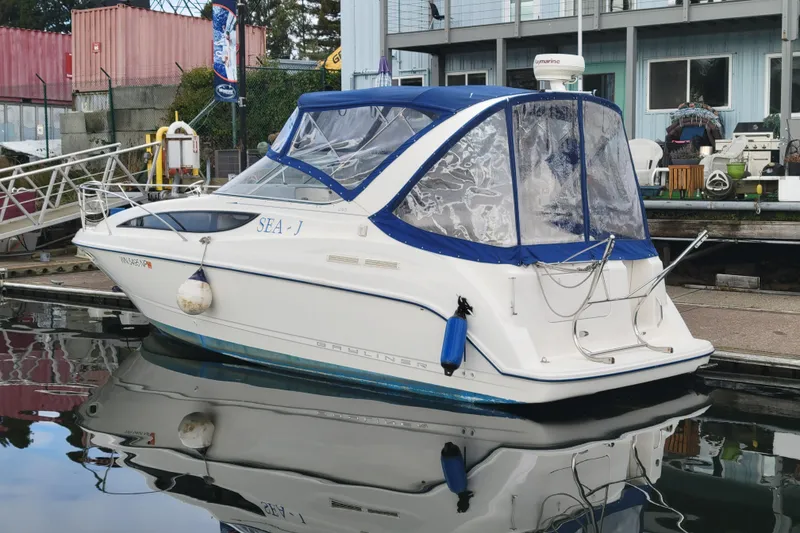 Slide: The Image of 2004 Bayliner 285 boat docked, featuring blue canopy and clear windows, reflecting on water. - 5