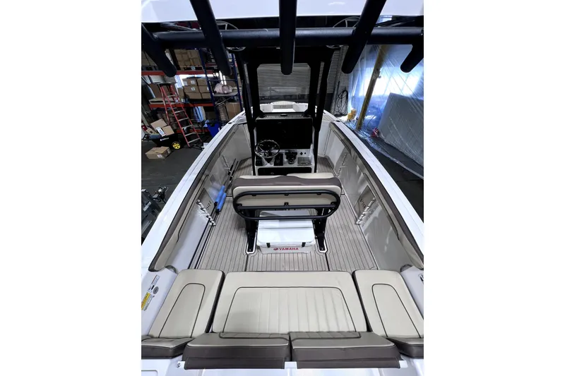 Slide: The Image of 2023 Yamaha Boats 255 FSH Sport E interior with seating and helm, in a warehouse setting. - 23
