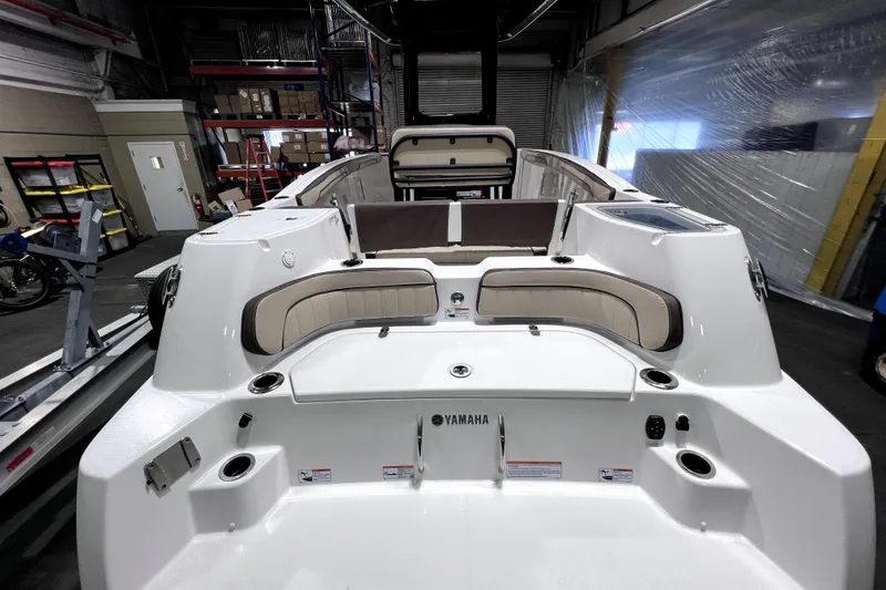 Slide: The Image of 2023 Yamaha Boats 255 FSH Sport E interior with seating and storage in a warehouse setting. - 8
