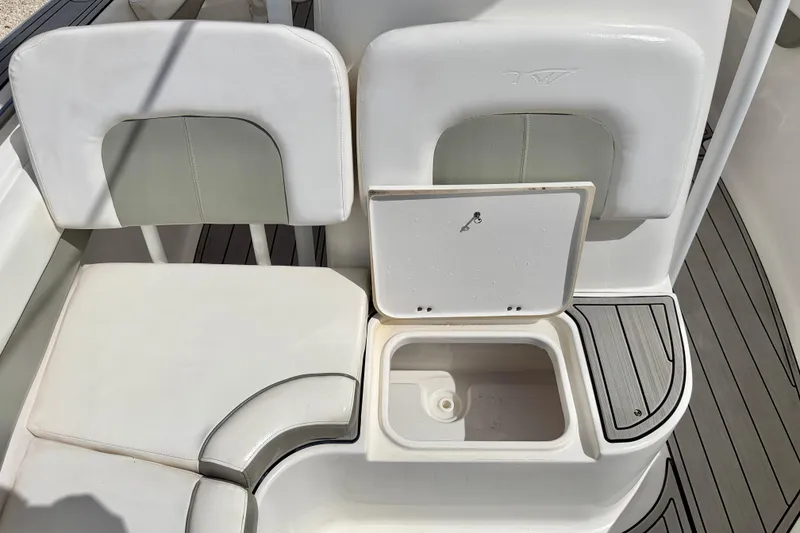 Slide: The Image of 2014 Tidewater 230 LXF boat seating with storage compartment, white upholstery, and deck flooring. - 14