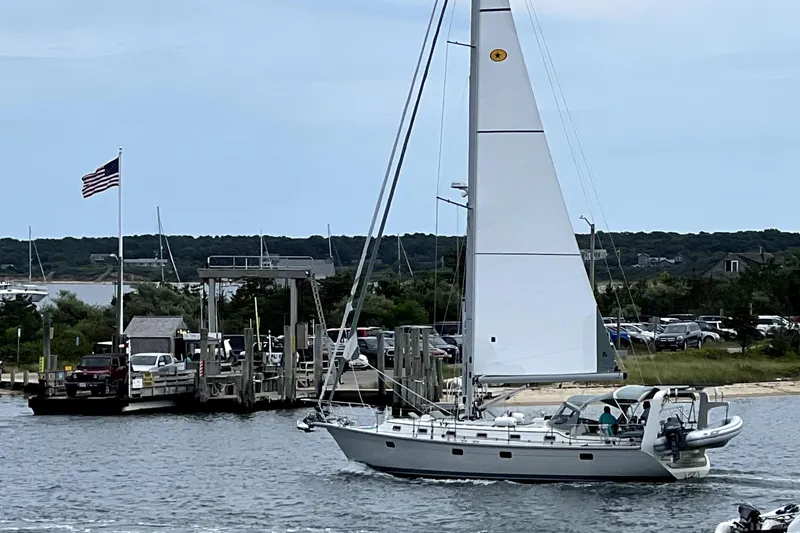 The Image of 2023 Island Packet 439 sailboat cruising near a dock with an American flag. - 0