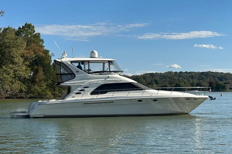 The Image of 2003 Sea Ray 560 Sedan Bridge yacht cruising on a serene lake under a clear blue sky. - 0