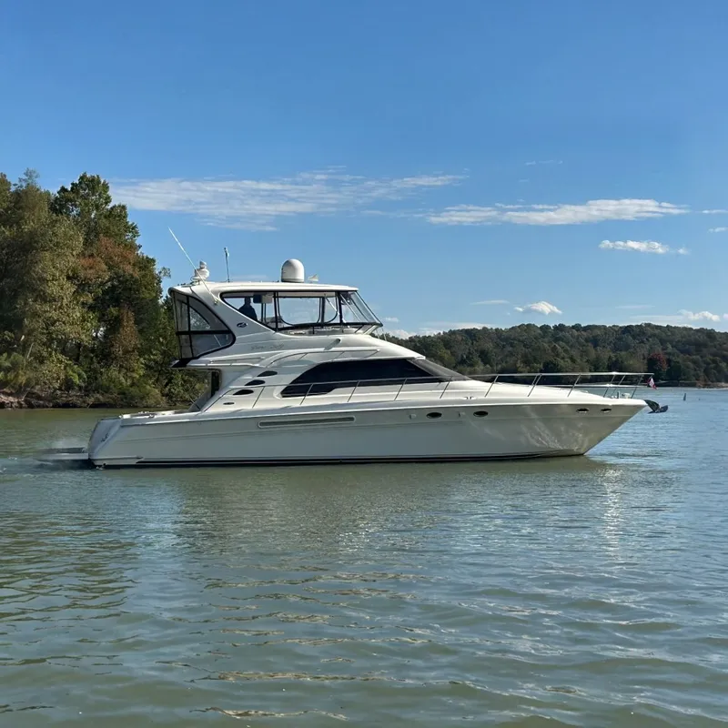 The Image of 2003 Sea Ray 560 Sedan Bridge yacht cruising on a serene lake under a clear blue sky. - 0