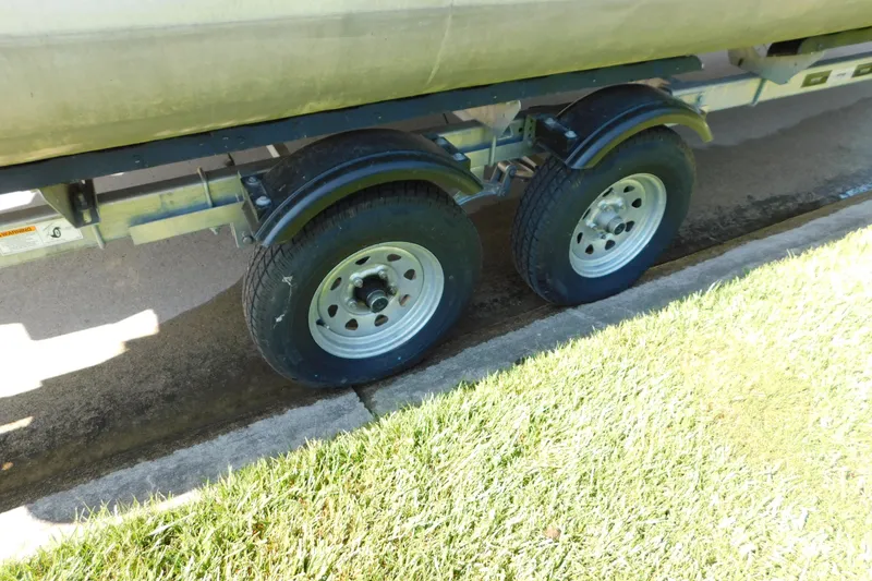 Slide: The Image of Trailer wheels of a 2023 Tahoe Pontoon 2385 LTZ Quad Lounger on grass. - 58