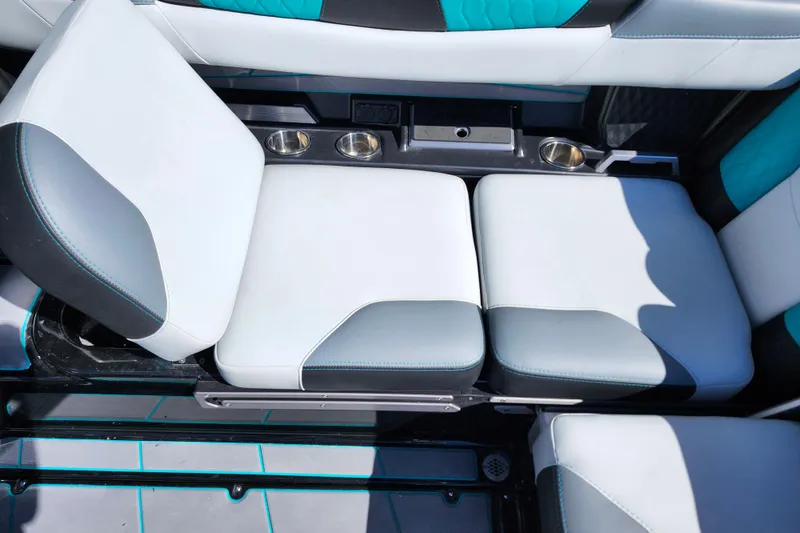Slide: The Image of 2022 Malibu M220 boat interior seating with cup holders, featuring white and teal upholstery. - 28