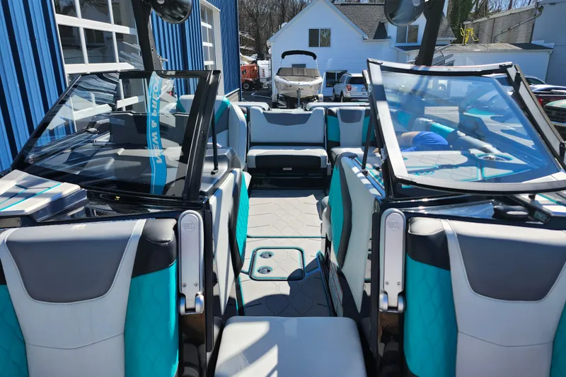 Slide: The Image of 2022 Malibu M220 boat interior with teal and gray seating, parked outdoors. - 49