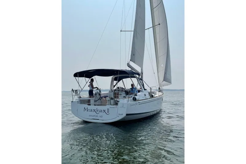 Slide: The Image of 2021 Beneteau Oceanis 38.1 sailboat on calm water, rear view with sails up. - 1
