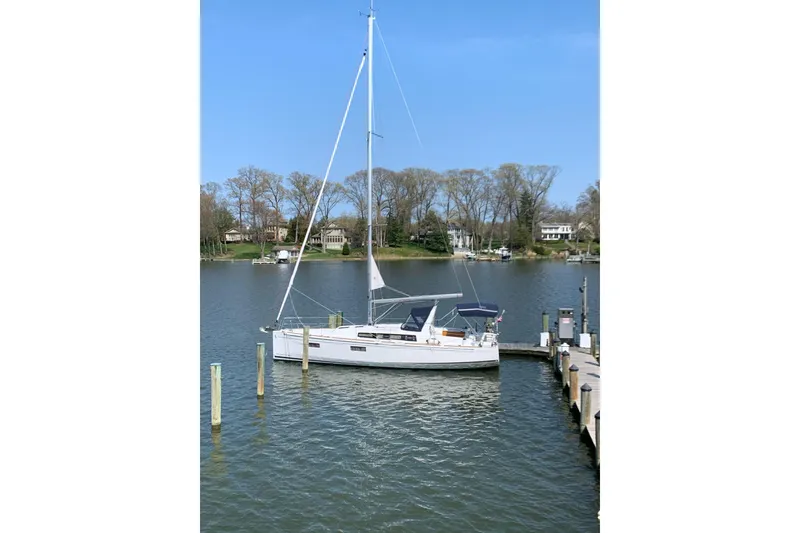 Slide: The Image of 2021 Beneteau Oceanis 38.1 sailboat docked on a serene lake with clear blue sky. - 2