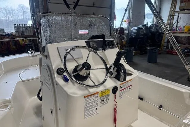 Slide: The Image of 2024 Boston Whaler 150 Montauk boat console with steering wheel and controls in a garage setting. - 7