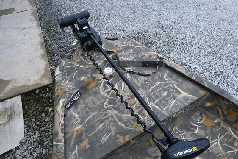 Slide: The Image of 2023 War Eagle 961 Blackhawk boat with camo design and trolling motor on gravel surface. - 9