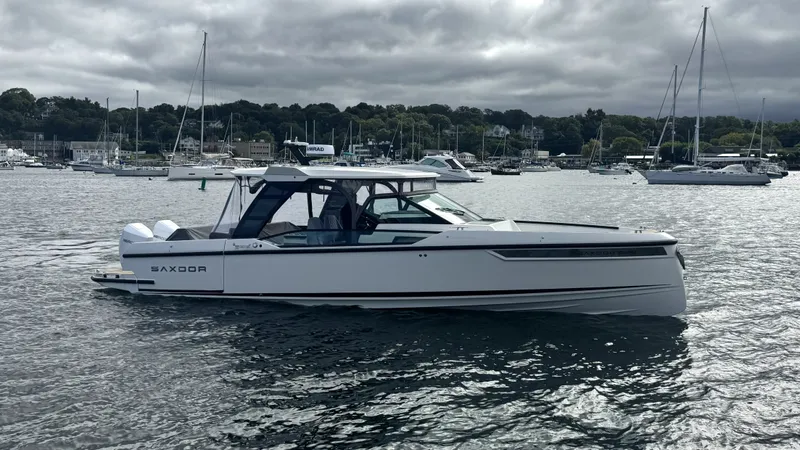 Slide: The Image of A 2027 Saxdor 320 GTO on calm water, surrounded by other boats and a wooded shoreline. - 42