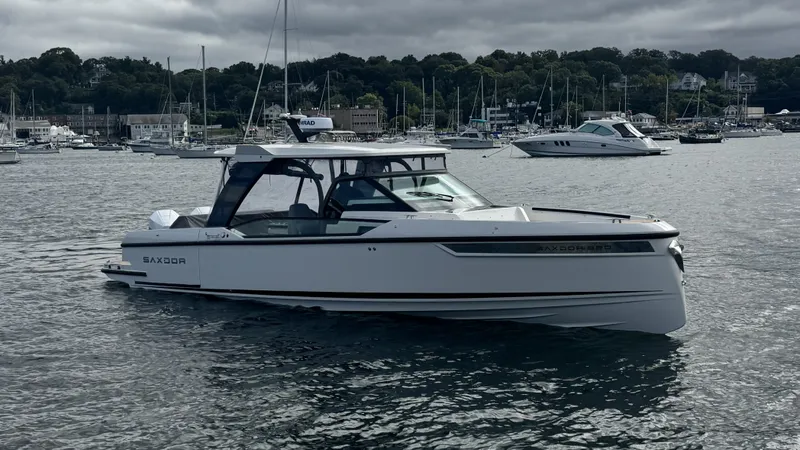 Slide: The Image of A 2027 Saxdor 320 GTO on calm water, surrounded by other boats and a wooded shoreline. - 41