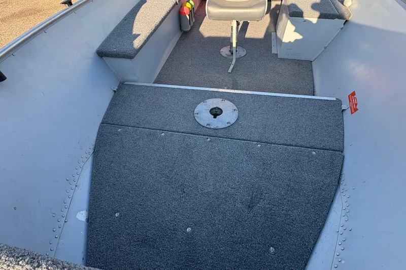 Slide: The Image of 1995 Lund 1440-V Rebel Tiller boat interior with gray carpeted flooring. - 10
