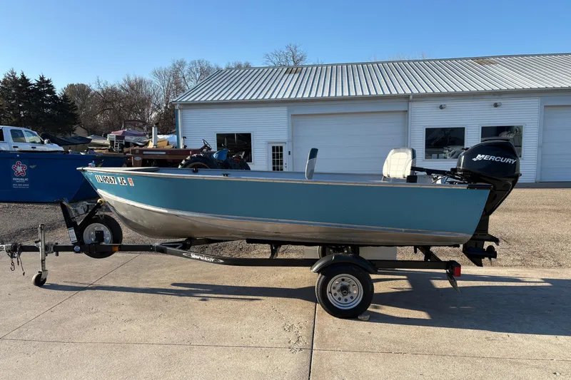Slide: The Image of 1995 Lund 1440-V Rebel Tiller boat on trailer, parked outside a garage. - 5