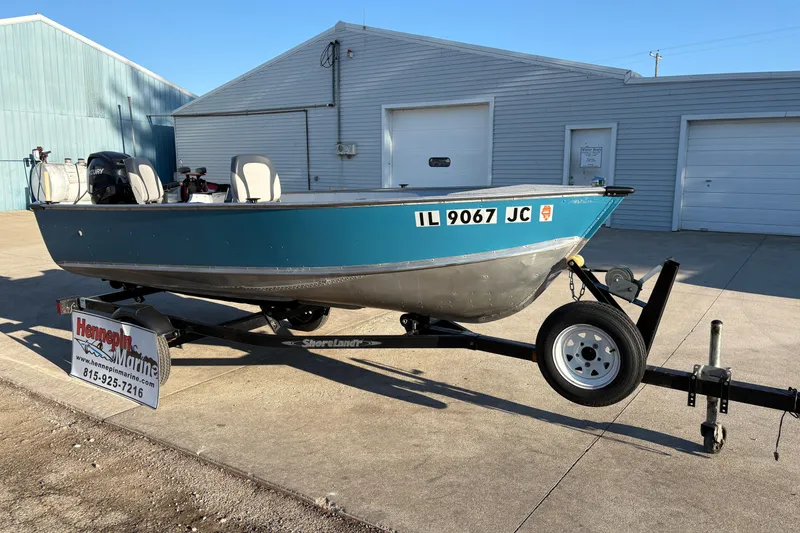 Slide: The Image of 1995 Lund 1440-V Rebel Tiller boat on trailer, parked outside a garage. - 8