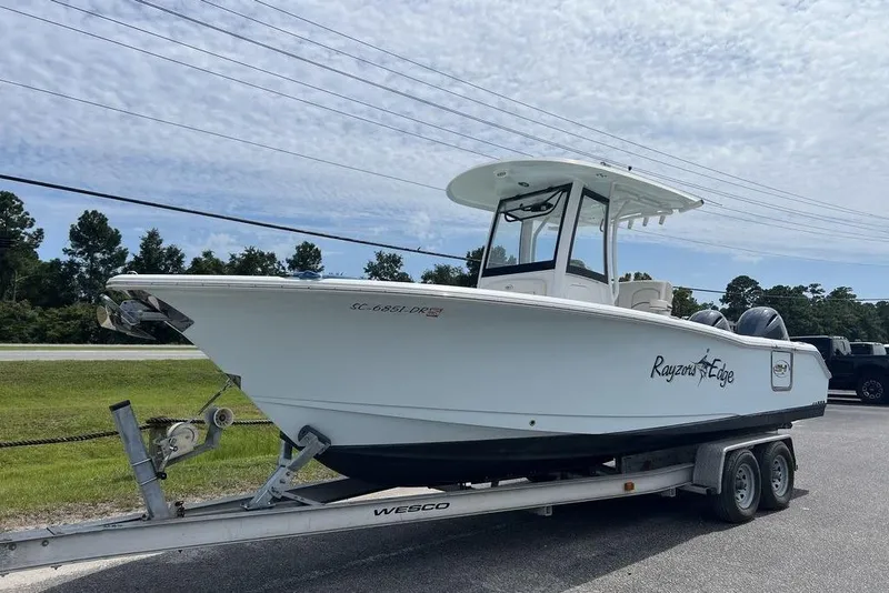 Slide: The Image of 2026 Sea Hunt Gamefish 25 boat on trailer, parked outdoors under a cloudy sky. - 2