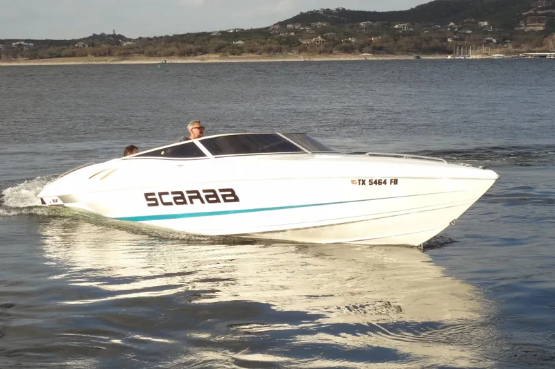 Slide: The Image of 1998 Wellcraft 26 Scarab speedboat cruising on a calm lake with scenic background. - 3