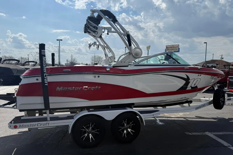 Slide: The Image of 2013 MasterCraft X10 boat on trailer, red and white design, parked outdoors. - 2