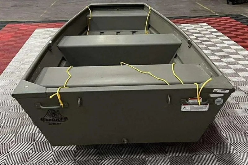 Slide: The Image of 2026 Tracker Grizzly 12 Jon boat on checkered floor, featuring durable design and yellow ropes. - 3