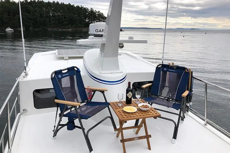 Slide: The Image of 2020 American Tug 362 deck with chairs, table, wine, and snacks, overlooking serene waters. - 8